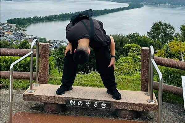 圖為「天橋立」美景的著名姿勢，當民眾背對山下的海上沙洲，低頭從自己的跨下朝後望時，會看到天地顛倒的畫面，沙洲就像一條向天上延伸的橋。 圖／讀者提供
