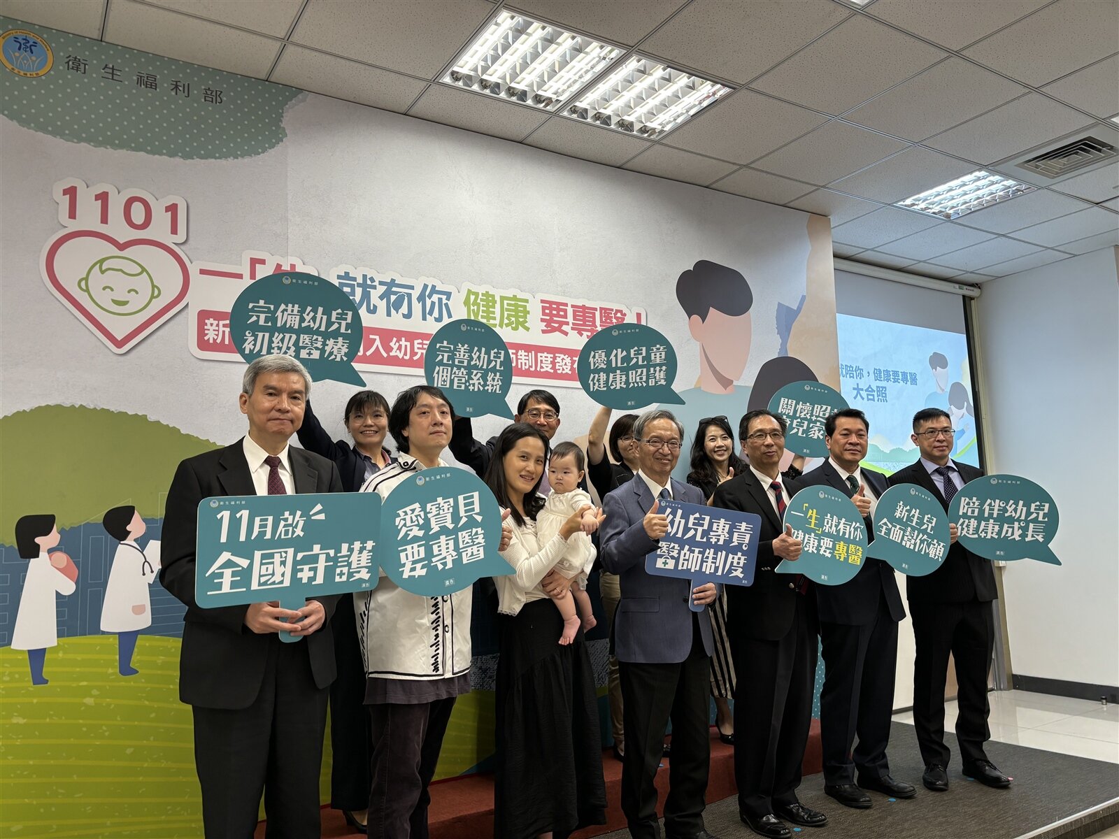 衛福部今舉辦新生兒全面納入幼兒專責醫師制度發布分享記者會,圖中舉藍色手板者為衛福部長薛瑞元、抱小孩者為楊媽媽。記者李青縈/攝影