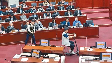 
台北市議員李傅中武（前右）11月30日在市政總質詢時，邀市長蔣萬安（前左）體驗騎乘電動滑板車，蔣搖搖晃晃差點撞上桌子。（劉彥宜攝）
