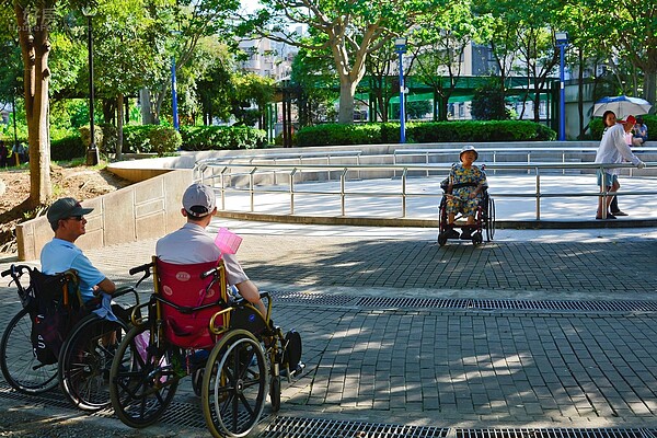 新北市中和區秀山公園,四點多時外傭看護帶著老人散步,另一名老人則被另一位不負責任的看傭扔在一旁睡覺,圖左下兩位健康精神狀況尚可的民眾神色自若的聊天中。(好房News記者 陳韋帆/攝影)