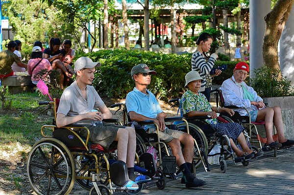 新北市中和區秀山公園,傍晚時外傭們將輪椅上的民眾一字排開,讓他們自己聊天,外傭們則聚集至後方聚會,僅剩一位盡責的看護仍陪著老人。(好房News記者 陳韋帆/攝影)