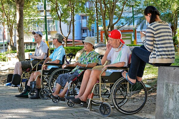 新北市中和區秀山公園,傍晚時外傭們將輪椅上的民眾一字排開,讓他們自己聊天,外傭們則聚集至後方聚會,僅剩一位盡責的看護仍陪著老人。(好房News記者 陳韋帆/攝影)