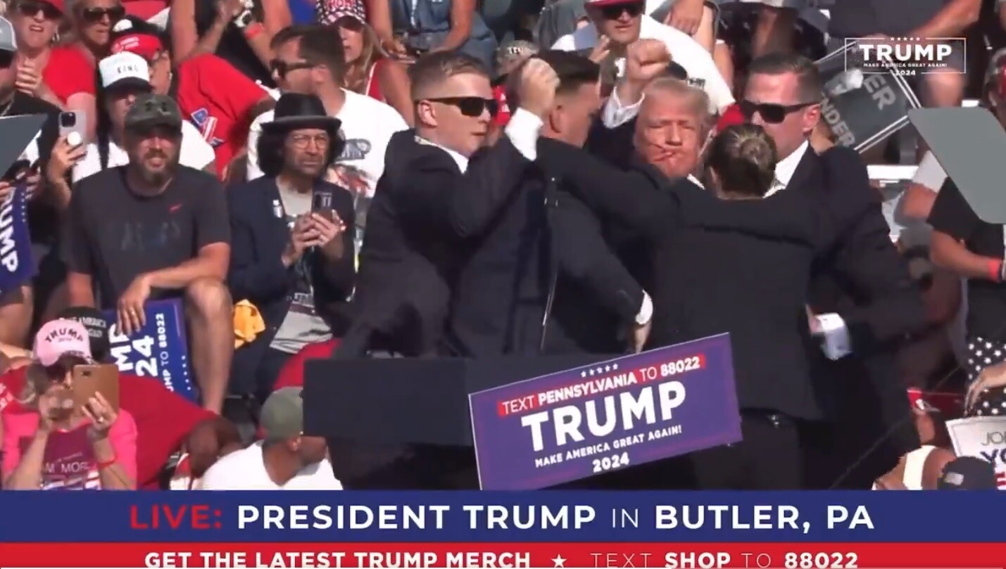 美國前總統、共和黨總統候選人川普在賓州宣傳造勢時遭槍擊,他一度蹲下,隨後在特勤人員的簇擁下重新起身並揚拳示意自己無恙,畫面中可見川普臉上有血漬。圖/翻攝自X @stoolpresidente