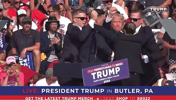 美國前總統、共和黨總統候選人川普在賓州宣傳造勢時遭槍擊,他一度蹲下,隨後在特勤人員的簇擁下重新起身並揚拳示意自己無恙,畫面中可見川普臉上有血漬。圖/翻攝自X @stoolpresidente