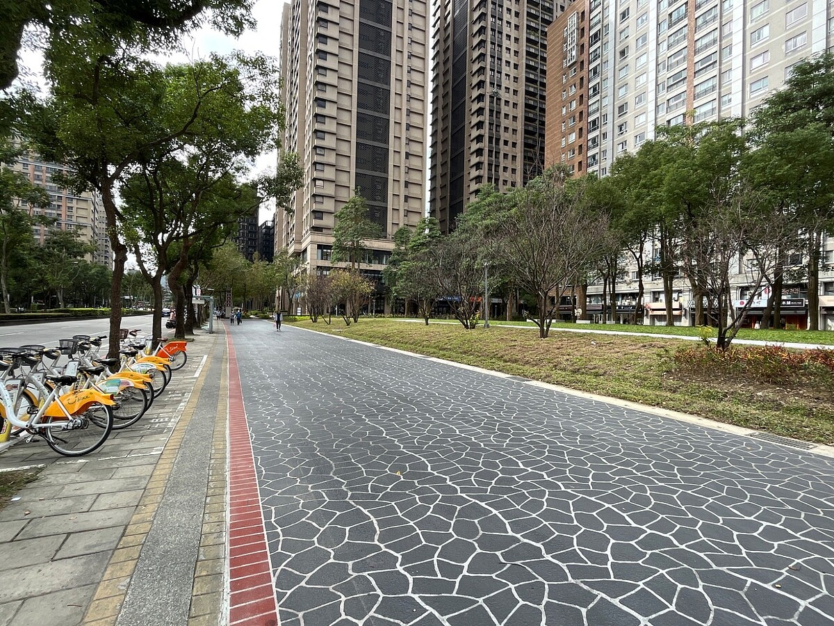 北大特區「草地公園」改善周遭人行道積水問題,並採用噴花地坪設計,與周邊公車站牌及YouBike微笑單車租借站銜接,為民眾提供舒適的步行環境。圖/新北市新工處提供