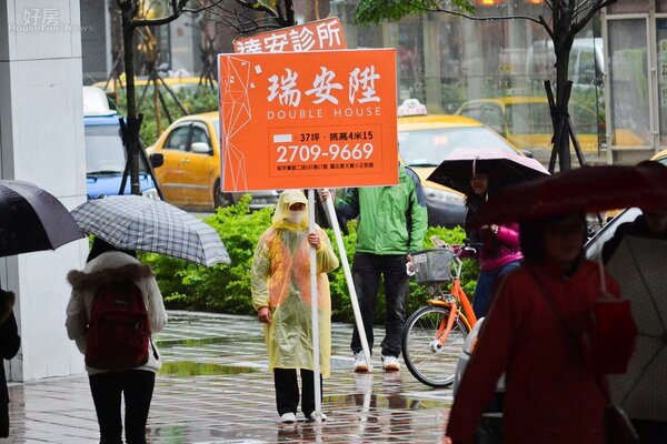 即使下雨天,在人潮眾多的地方,也時常看見舉牌工人穿著雨衣站在交通要道 宣傳建案廣告。(好房News記者 陳韋帆/攝影)
