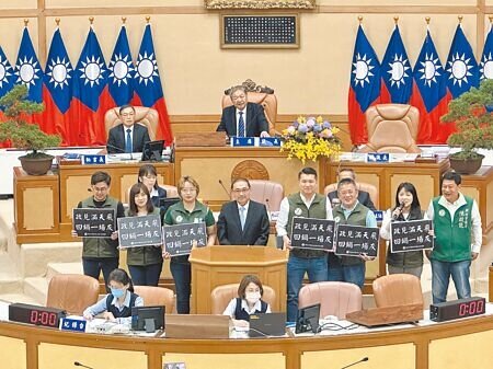 
新北市議會11日進行市政總質詢，民進黨議員李宇翔（二排右四）、黃淑君（二排左三）、陳乃瑜（二排左二）等人高舉「政見滿天飛、回鍋一場灰」手牌，諷刺新北市長侯友宜（二排左四）政見跳票。（高鈞麟攝）
