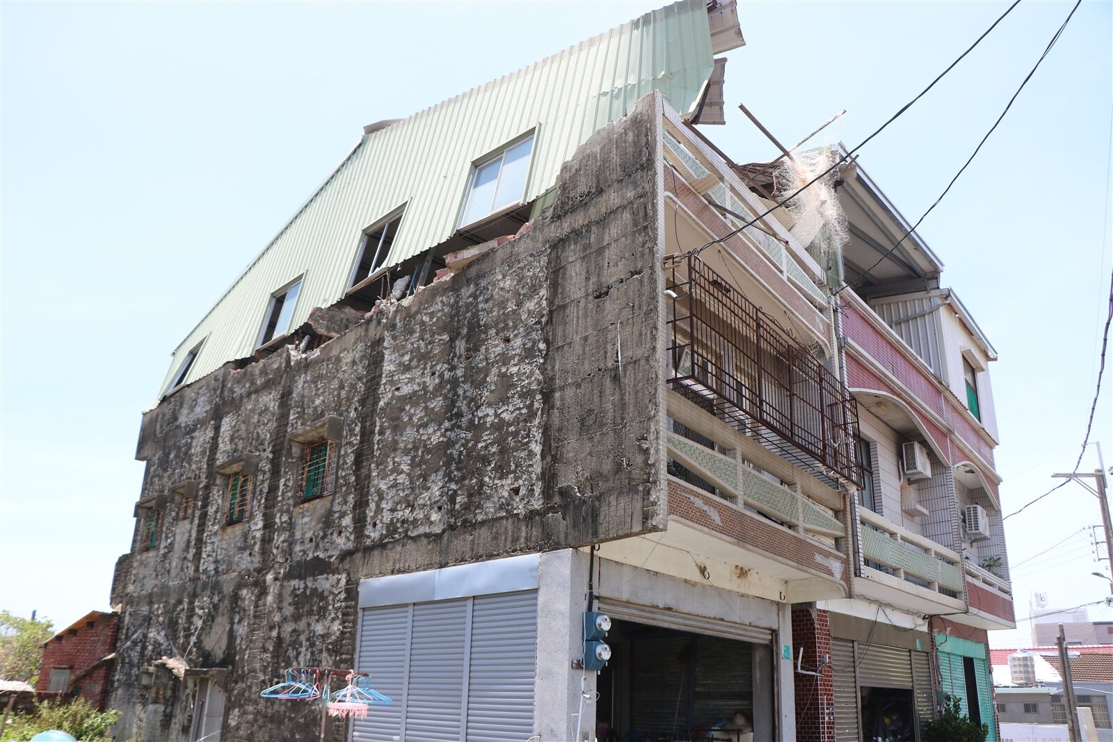 台南七股龍山里一處民宅3樓鐵皮加蓋遭颱風吹歪,鐵皮建築倒塌緊貼靠在鄰宅牆面,迄今已過10多天,屋主母子倆平時都需洗腎,面對房屋受損無能為力,當地里長也希望能有專業人士協助幫忙處理危險鐵皮。記者萬于甄/攝影