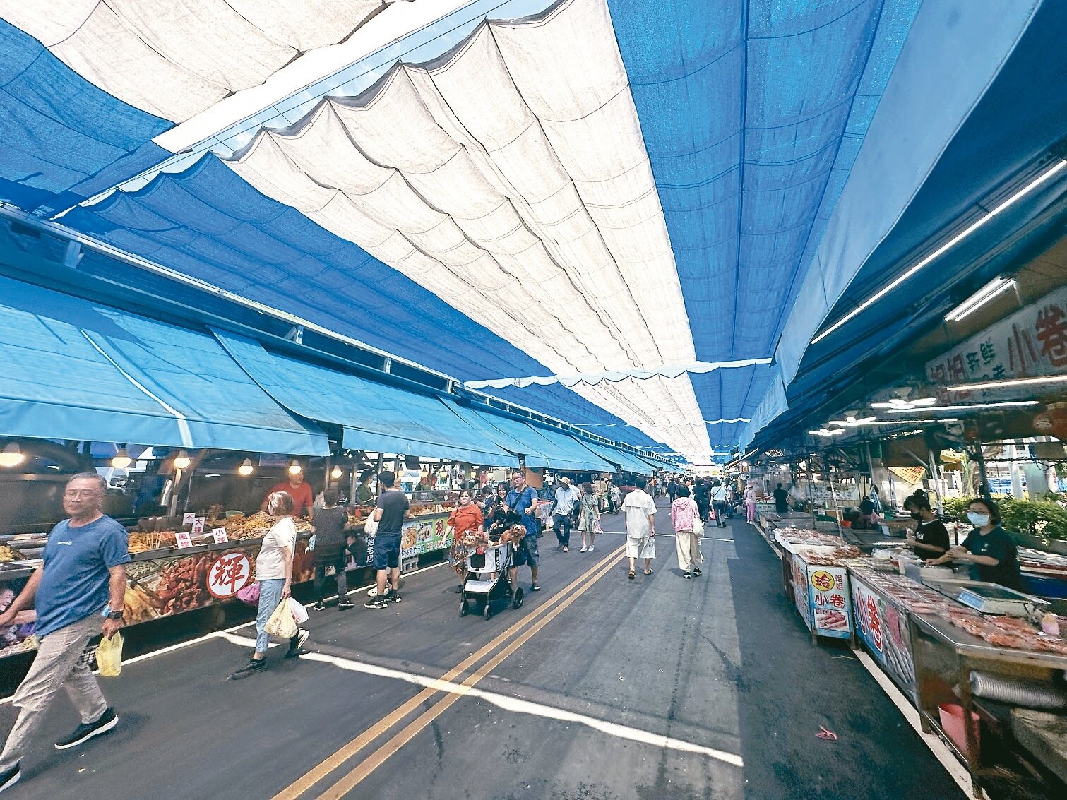 高雄興達港觀光漁市建沿街遮陽帆布，吸引遊客假日優閒逛街採買魚貨，不過有一段路沒裝設遮陽帆布 。記者巫鴻瑋／攝影 