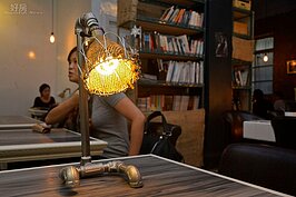 工業風簡陋外牆外，少不瞭鋼鐵系的擺飾，此水管燈是老板王凱文自己手做的，燈罩則使用做為椅套的麻布袋廢料製作而成，與店內裝潢完全融為一體。