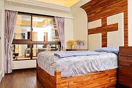 有別於客廳的陽剛味，主臥室盡現女主人的溫婉。整面牆是由團隊自製白色系雕花衣櫃，細膩的質感讓主臥房洋溢幸福浪漫，收納空間的巧妙安排，滿足夫妻倆日常所需。視覺從衣櫃延伸到另一道牆面，隱形門內是更衣室及淋浴間，整面牆都以噴漆、烤漆處理，不但質感升級，只需以抹布擦拭保養，清潔更方便。