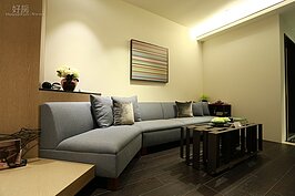 三加二配置的沙發座椅不採L型排列，而是略為呈現弧形的方式，這是為了讓進屋之後的動線更為流暢。灰色的沙發搭配白色的牆面，整體來講就是一個極簡風。燈具部分也揚棄主燈的傳統概念，而是以嵌燈來當照明。