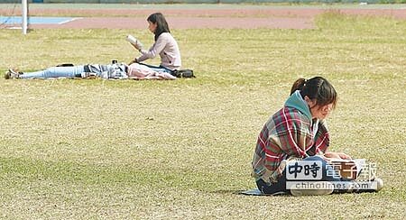 早晚氣溫偏低,高雄考區有考生及陪考親友乾脆坐在操場上,邊看書邊享受溫暖的陽光。(謝明祚攝)