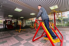 小孩在兒童遊憩區嬉戲，大人也有簡易的健身器材可以使用。