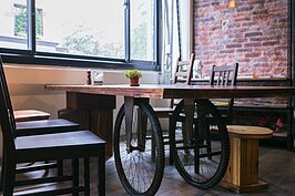 三輪車的輪子搖身一變成為餐桌的桌腳。襯印著後面牆上毫無修飾的紅磚牆，彷如讓人進入當年美軍在台時的風華年代。